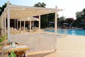 Un espace extérieur abrité avec des tables et des chaises, une piscine et des parasols.