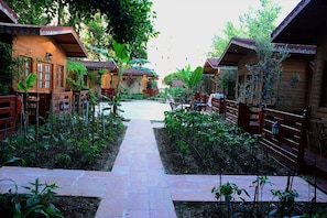 Un sendero conduce a cabañas de madera, con un jardín a cada lado.