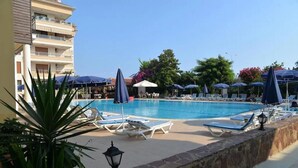 A swimming pool with lounge chairs and umbrellas, surrounded by a stone wall and potted plants. - Şevki Bey Hotel (Alanya)