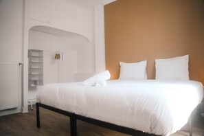 Ein Schlafzimmer mit einem Bett, weißer Bettwäsche, Holzboden, einem weißen Kleiderschrank und einer braunen Akzentwand.
