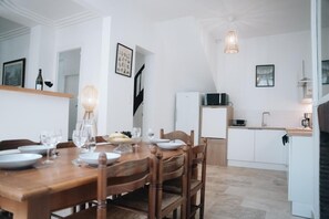 Ein Essbereich mit Holztisch, gedeckt für vier Personen, einem weißen Kühlschrank und einer Küchenzeile mit weißen Schränken und einer Mikrowelle.