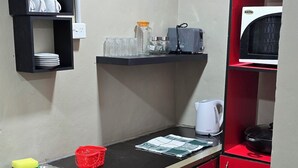 A compact kitchen with red cabinets, a black countertop, and a microwave. There are shelves with cups and a kettle. - SN Flats Nadera (Suva)