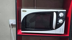 A compact kitchen with a red cabinet housing a white microwave and two black frying pans on a lower shelf. - SN Flats Nadera (Suva)
