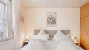 Una cama doble con cabecera, mesitas de noche con lámparas, una obra de arte enmarcada sobre la cama y un armario de madera.