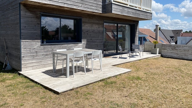 A modern house with a wooden exterior, a balcony, and a patio with outdoor furniture.