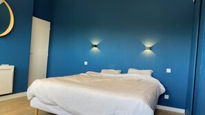 A bedroom with a large bed, two wall-mounted lights, a round mirror, and a white radiator.