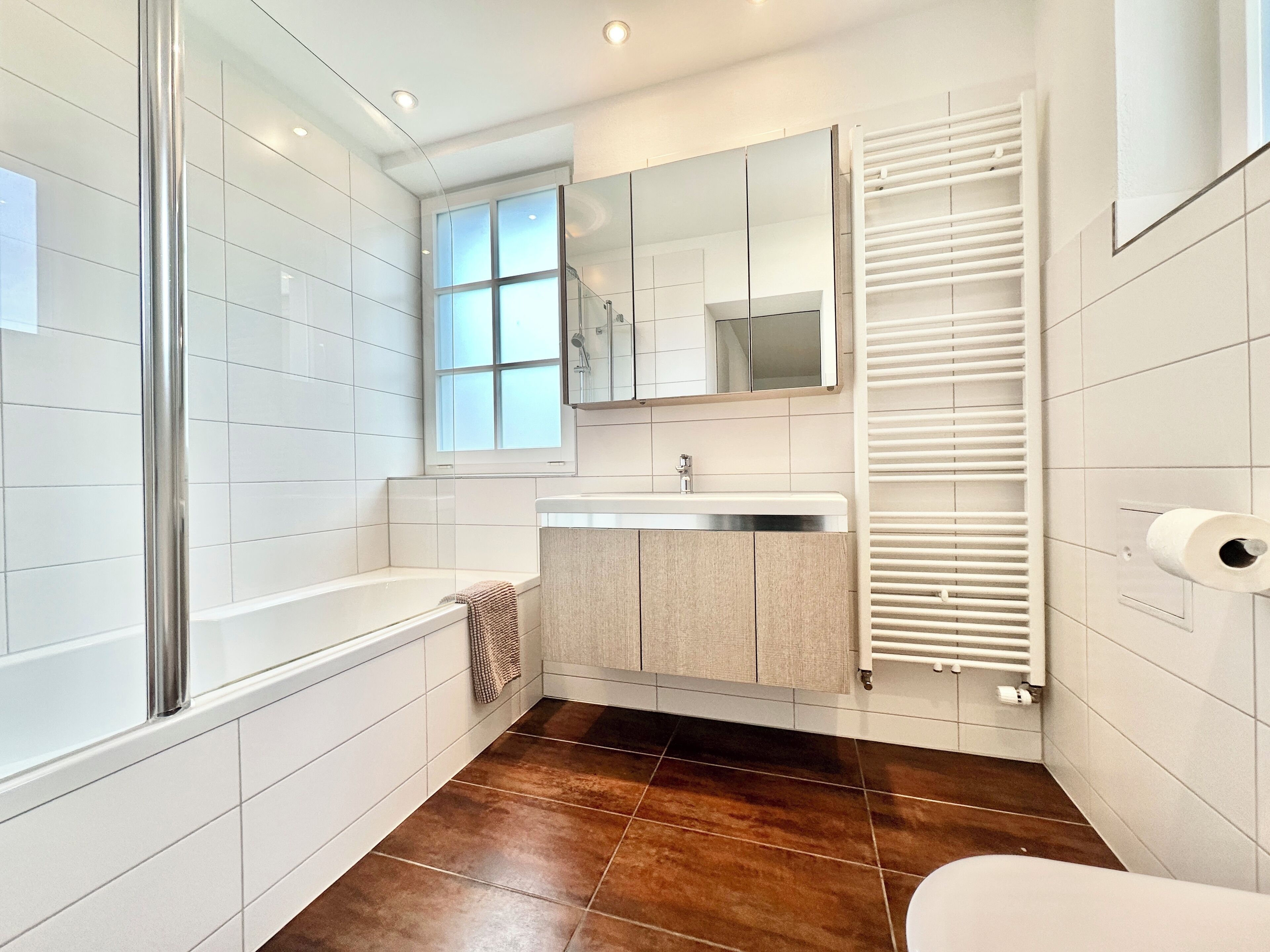 A modern bathroom with a bathtub, a sink, a mirror, and a towel rack.