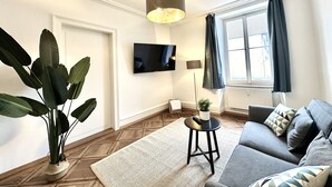A modern living room with a flat-screen TV, a large plant, a grey sofa, and a patterned rug. - Business Apartment Derendingen (Derendingen)
