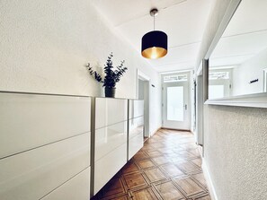 Een hal met een houten vloer, witte wanden en een hangende吊灯.