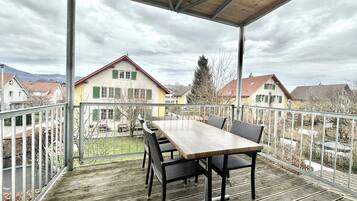 A covered outdoor area with a table and chairs, overlooking a residential neighborhood with houses and mountains in the background.