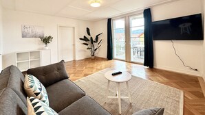 A living room with a sofa, a small table, a plant, and a TV on the wall. - Business Apartment Derendingen (Derendingen)