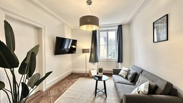 Ein modernes Wohnzimmer mit Flachbildfernseher, grauem Sofa, rundem Couchtisch und einer großen Pflanze.