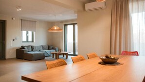 Un salon moderne avec un canapé, une table à manger et des chaises. On y trouve une fenêtre avec des rideaux, un appareil de climatisation et un luminaire au plafond.