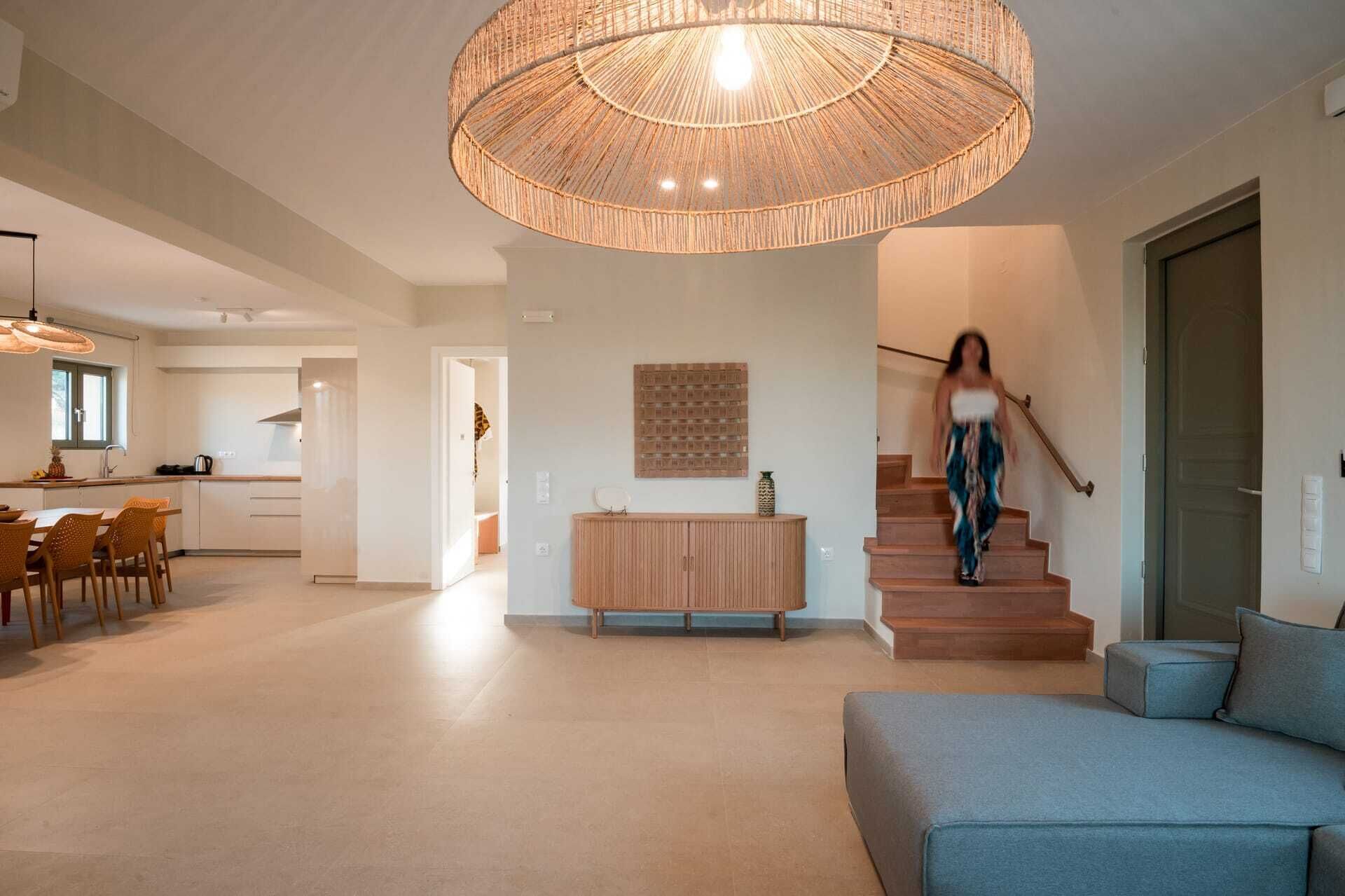 Un vaste espace de vie agrémenté d’un grand luminaire en fibres tressées, d’un escalier en bois et d’un canapé bleu.
