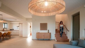 Un vaste espace de vie agrémenté d’un grand luminaire en fibres tressées, d’un escalier en bois et d’un canapé bleu.