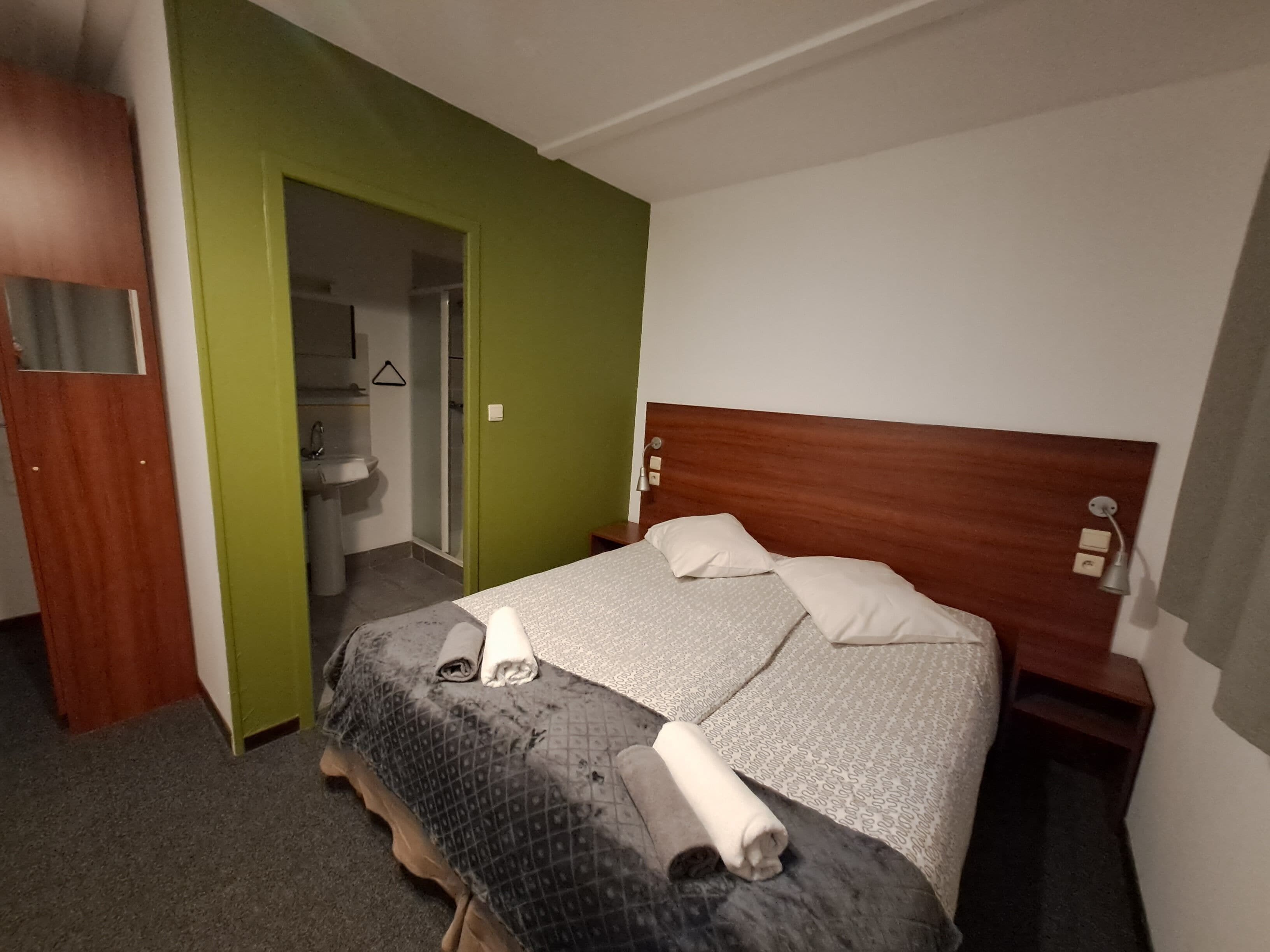 Ein Hotelzimmer mit einem Bett, einem hölzernen Kopfteil, einem Nachttisch und einer grünen Wand.
