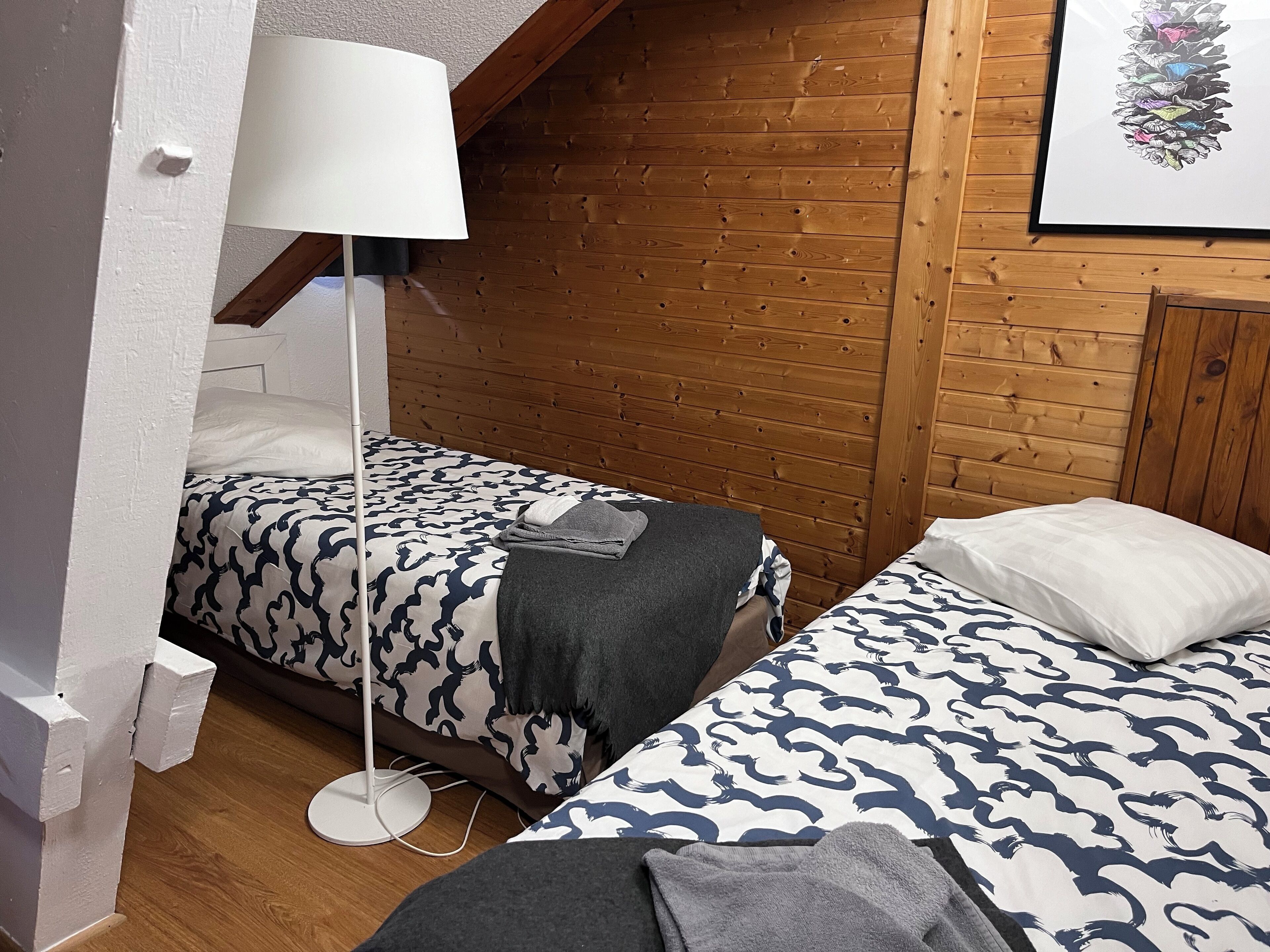A room with two beds, a standing lamp, and a wooden wall.