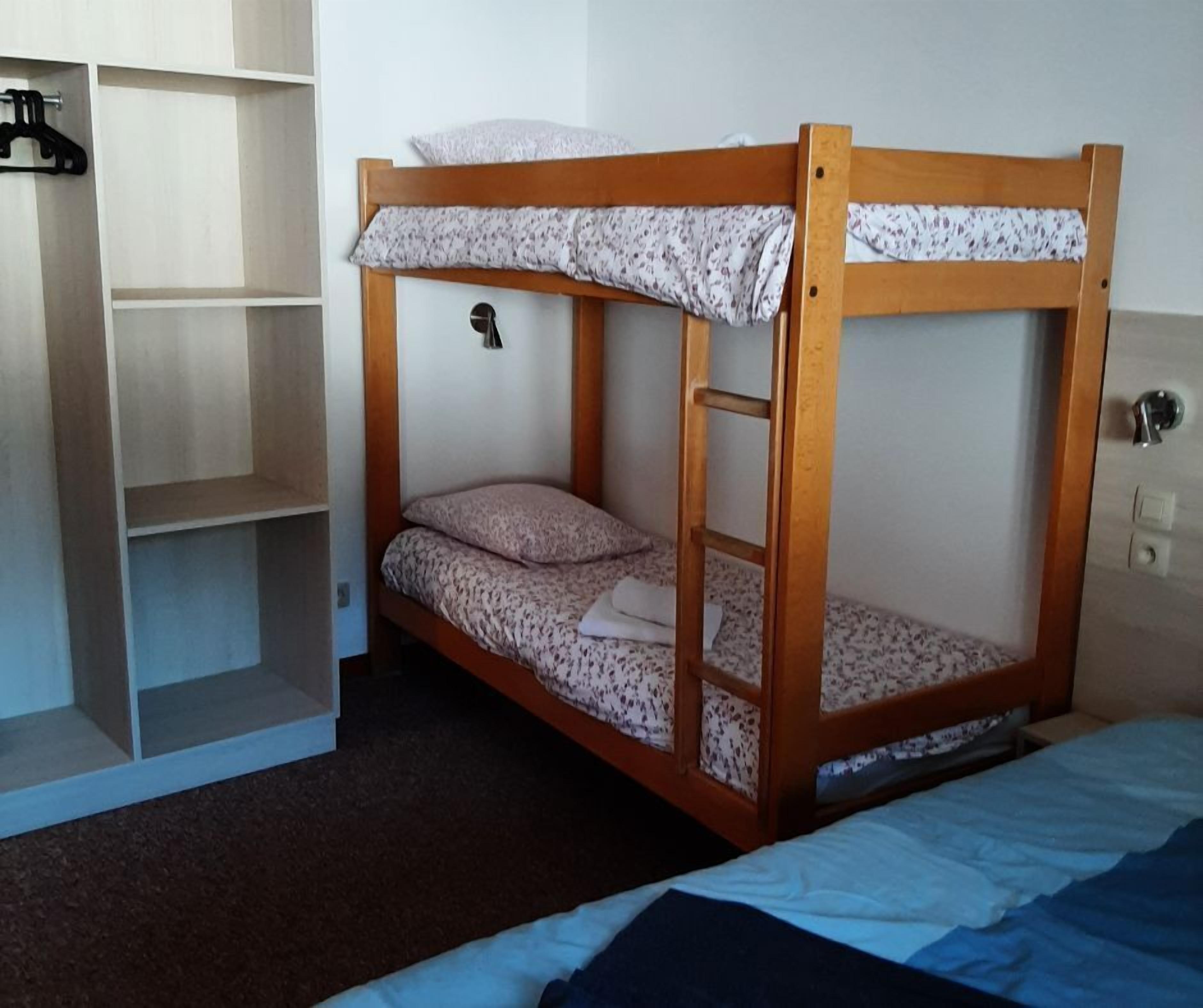 A bunk bed with a wooden frame, a small shelf unit to the left, and a door with a handle on the right.