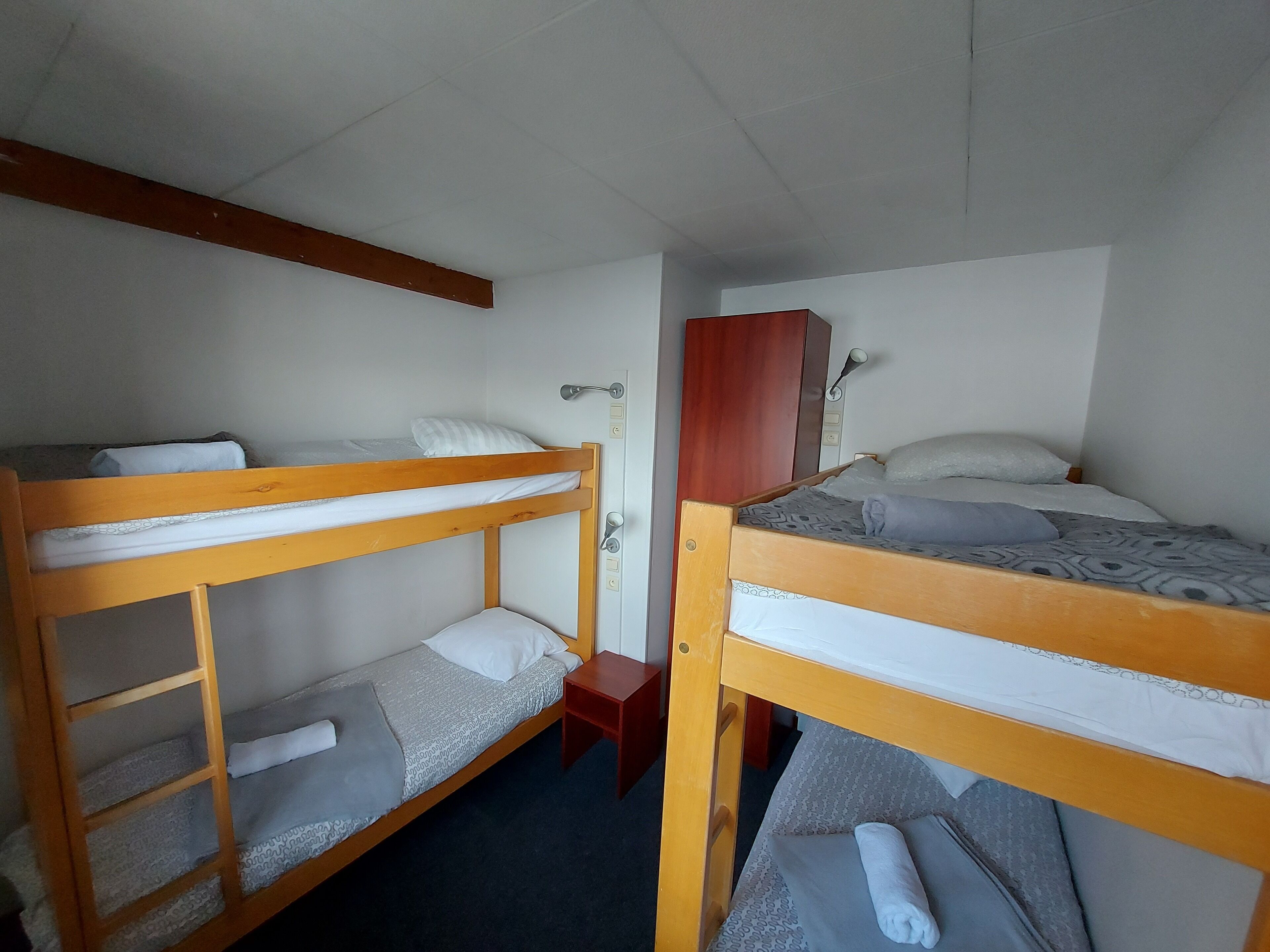 A room with two bunk beds, a wooden wardrobe, and a small table.