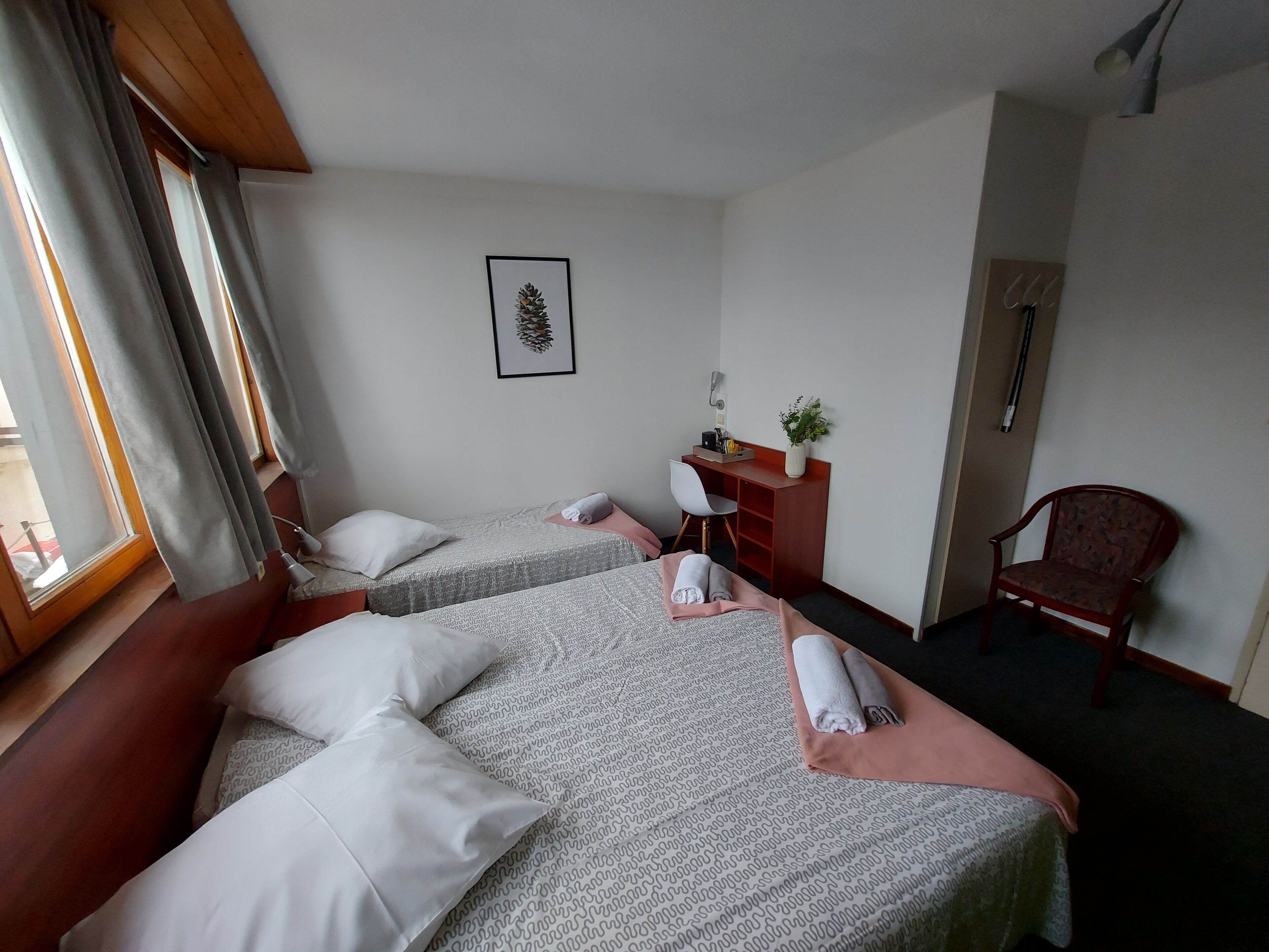 A hotel room with two beds, a desk, a chair, and a window with curtains.