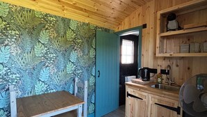 Un intérieur en bois comprenant une table à manger, des chaises, un coin cuisine avec un évier et un ventilateur.
