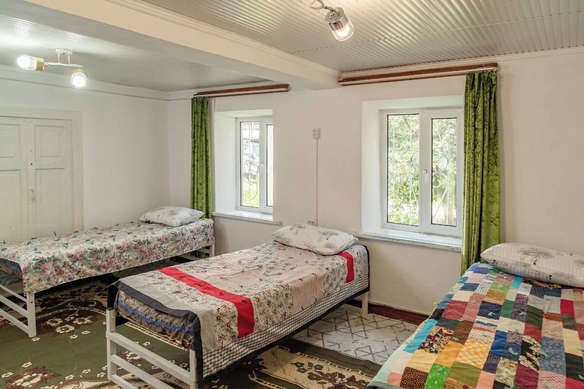 A room with two single beds, a window with curtains, a ceiling fan, and a door.