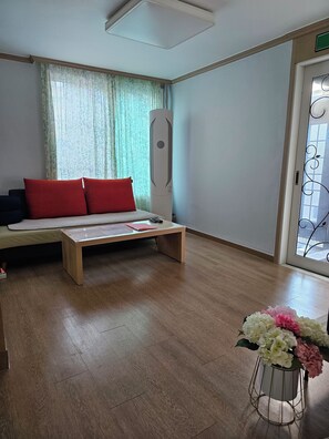 Um quarto com cama, mesa de cabeceira, janela com cortinas, radiador, porta com portão de metal e um vaso com flores.