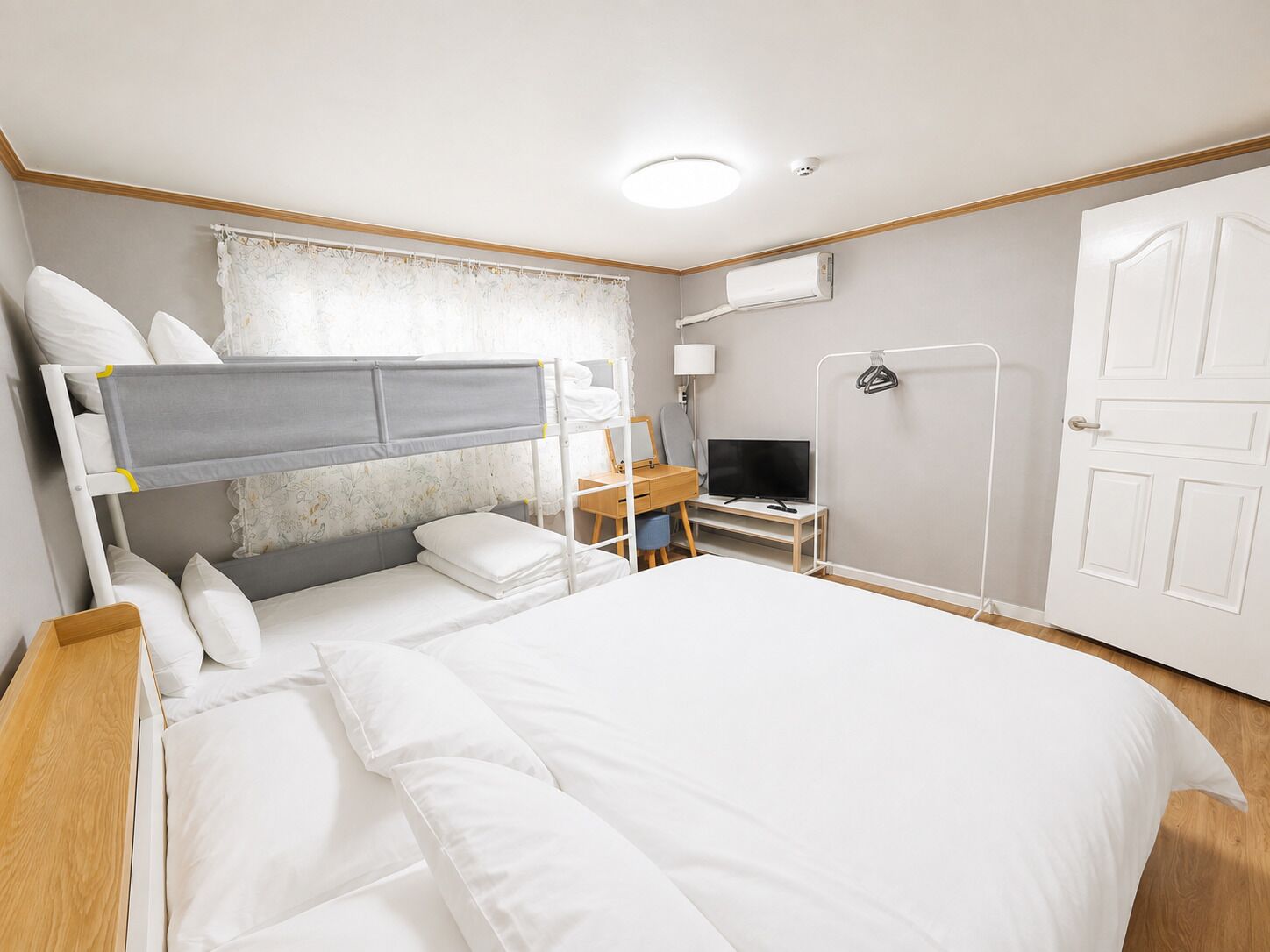 A hotel room with a bunk bed, a desk with a computer, a TV, and a door.