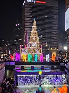 Een felverlichte kerstboom met een ster bovenop, omringd door verlichte figuren en een waterpartij.