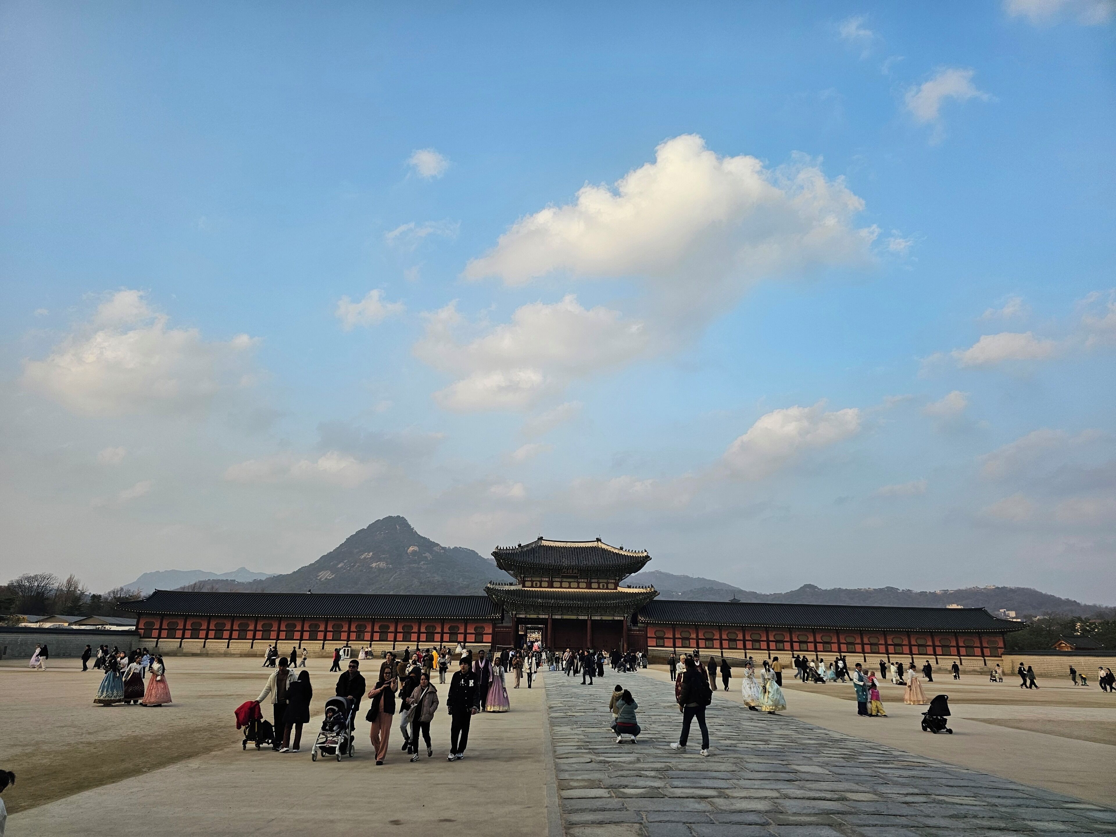 A large open courtyard with traditional architecture, a prominent gate, and mountains in the background.