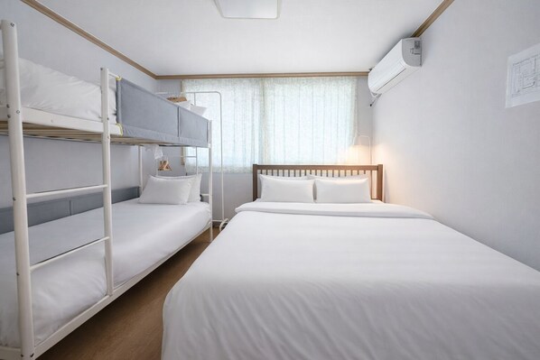 Ein Hotelzimmer mit Stockbetten, einem großen Bett und einem Fenster mit Vorhängen.