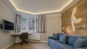 A modern living room with a wooden accent wall, a blue sofa, a desk with a chair, and a TV mounted on the wall. - Kamperhof, App. 5 - Modern vacation apartment with 3 rooms on approx. 87 m², for max. (Sylt)