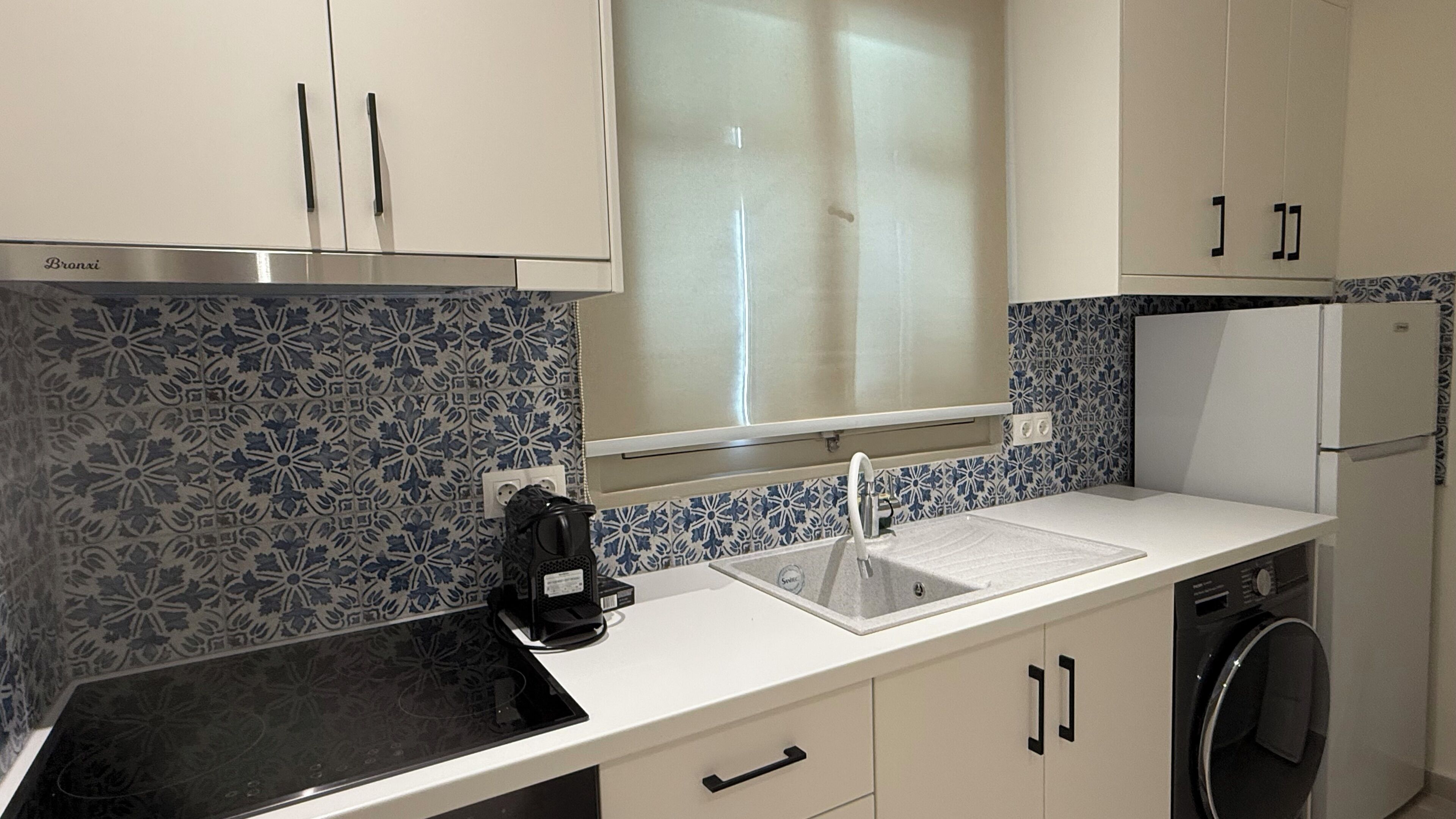 A kitchen with a stainless steel range hood, a sink with a faucet, a coffee maker, and a washing machine.