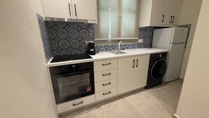 A compact kitchen with a built-in oven, a coffee maker, and a washing machine. - Family Apartment, Ammos Skiathos (Skiathos)