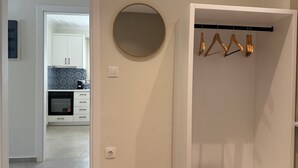 A modern kitchen with white cabinets, a built-in oven, and a coffee maker. There is a round mirror on the wall and a coat rack with wooden hangers. - Family Apartment, Ammos Skiathos (Skiathos)