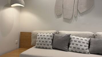 Una sala de estar moderna con un sofá, cojines estampados, una lámpara colgante y un estante fijado a la pared.