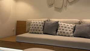 A modern living room with a beige sofa, patterned cushions, a round ottoman, and abstract wall art. - Family Apartment, Ammos Skiathos (Skiathos)