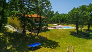Una casa con piscina, cancha de tenis y jardín cubierto de césped.