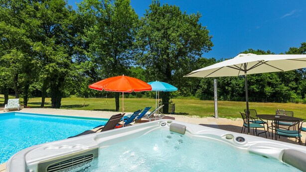 Un jacuzzi con sillones reclinables, una piscina y sombrillas.