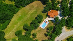 Vista aérea de una propiedad con piscina, un césped amplio y una casa con techo rojo.
