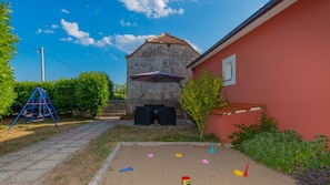 Un patio con un edificio de piedra, un columpio y una pequeña zona de juegos con juguetes.