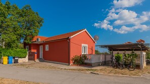 Et rødt hus med tegltag, parabolantenne og en cykel parkeret udenfor.