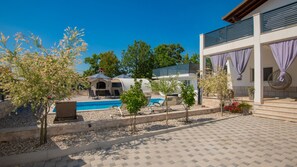 A pool area with lounge chairs, a small building with a sloped roof, and a modern building with a balcony.
