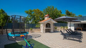 A backyard with a trampoline, a stone-built barbecue area, and outdoor seating.