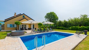 Une piscine avec des chaises longues et des parasols, une maison à la façade jaune et une pelouse bien entretenue.