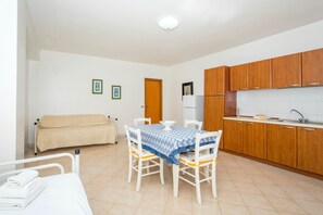 Une pièce de taille modeste comprenant une table à manger, des chaises, un lit, un coin cuisine et une porte.