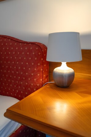 A lamp on a wooden bedside table next to a bed with a red pillow. - Room '5' with Shared Garden and Wi-Fi (St Blasien)