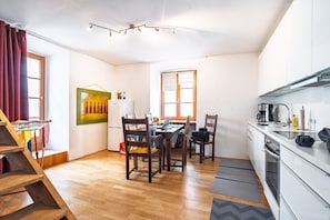 A compact kitchen with a dining area, wooden chairs, a table, and a painting on the wall.
