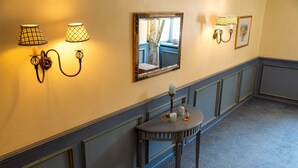 Un couloir avec une table ronde, des appliques murales, un miroir et un tableau encadré.