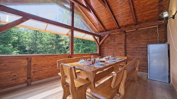 Una mesa de madera con sillas, un refrigerador y un ventanal con vistas a árboles.